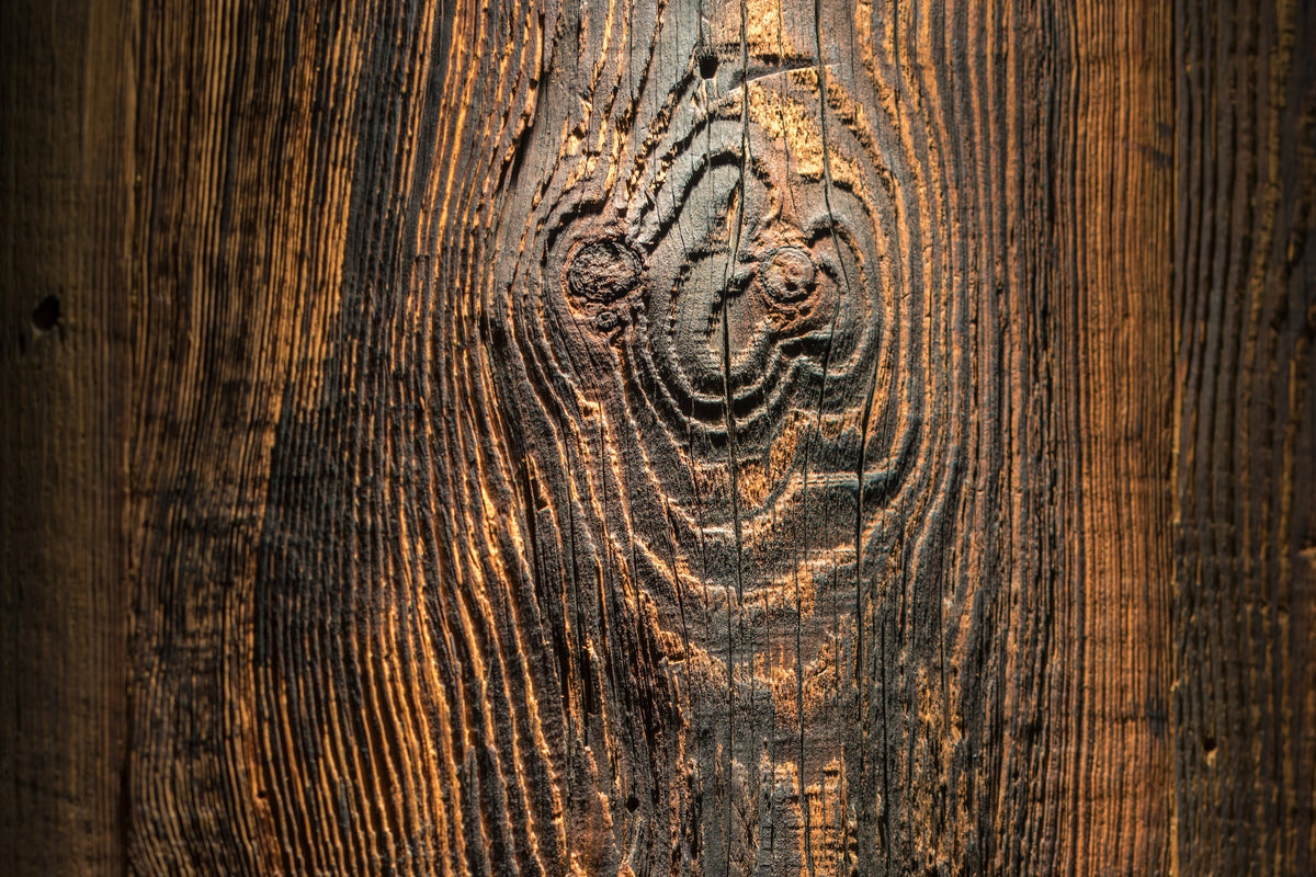 Close-up of a dark rustic reclaimed  wood surface with prominent grain, knots, and a warm golden-brown highlight running vertically through the center.