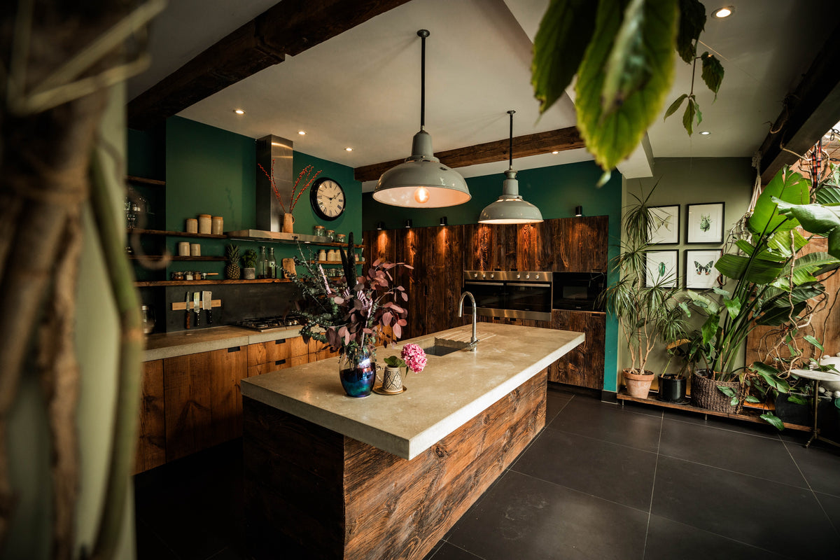 reclaimed barn wood kitchen with a large island concrete worktop green walls hanging lights and indoor plants in a uk home