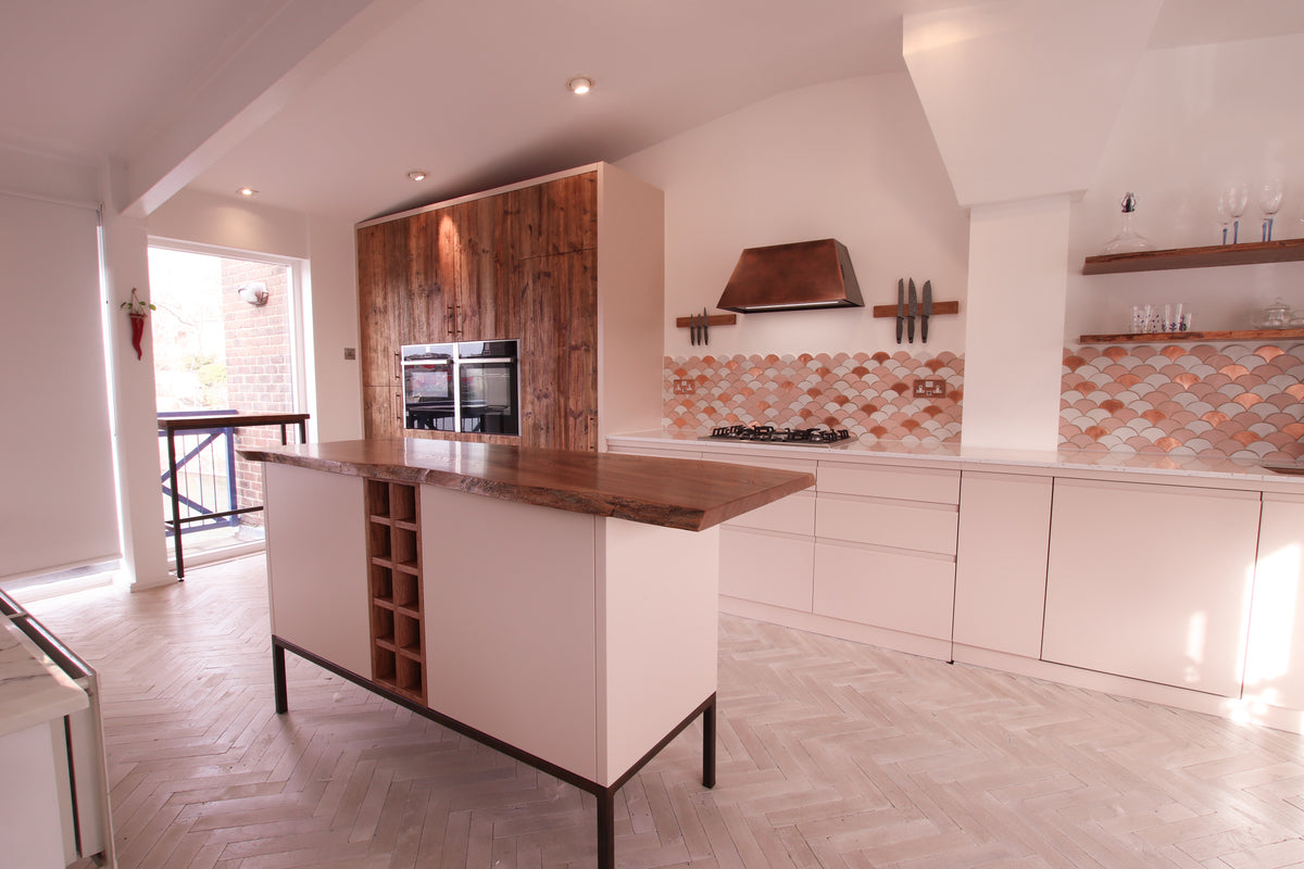 Full view of a blush kitchen with a reclaimed barn wood tall unit, matching island with timber top, and scalloped tile backsplash