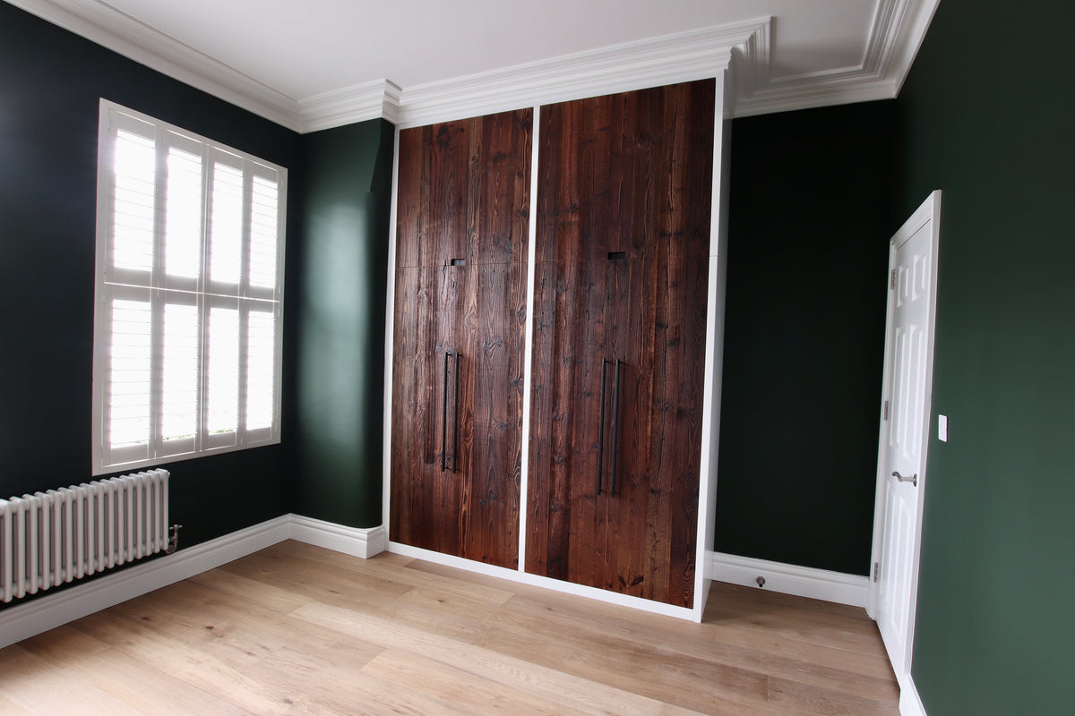 Bespoke fitted wardrobe with dark green reclaimed barn wood doors framed in white, set against deep green walls in a modern bedroom