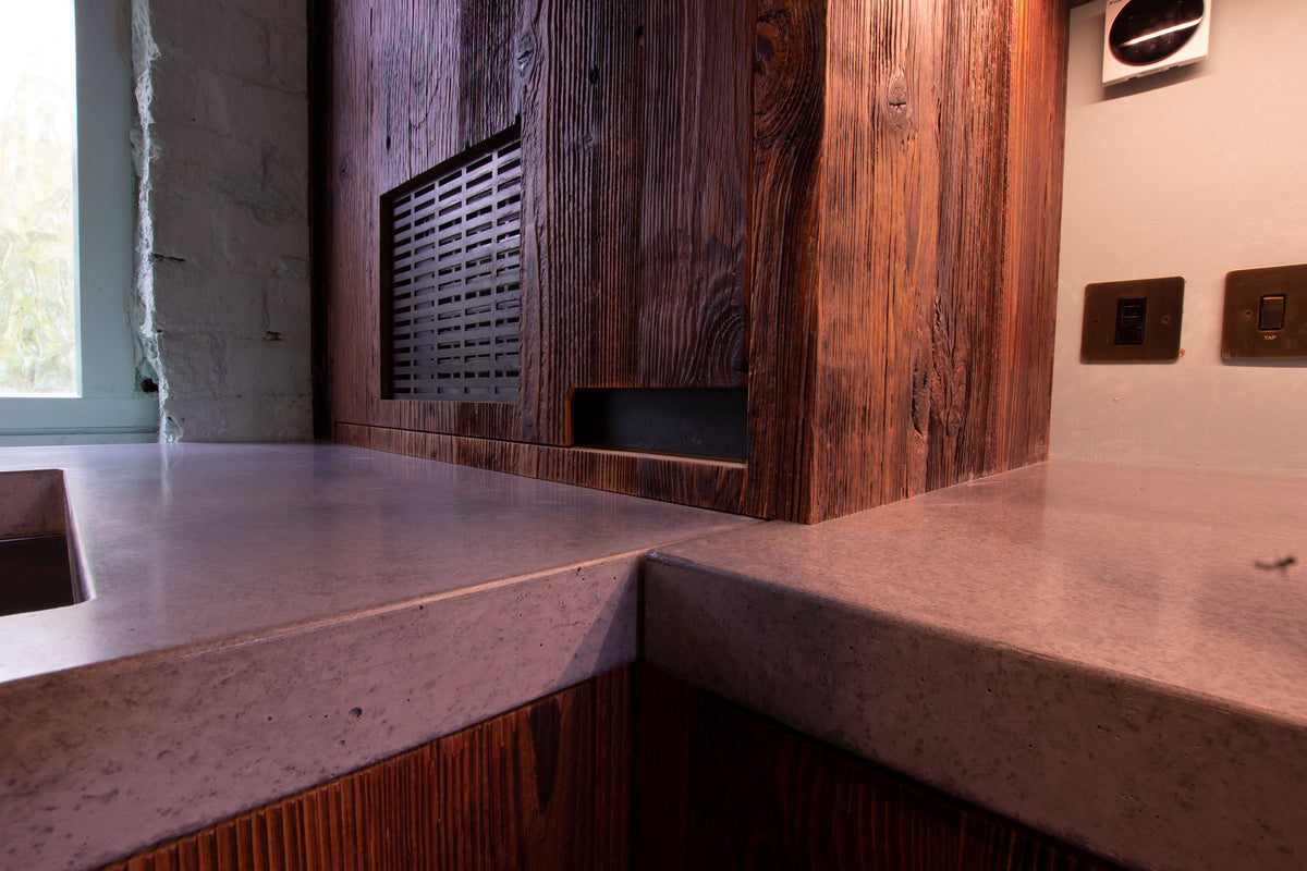 Kitchen sink area featuring a matte black tap, concrete worktops and reclaimed barn wood cabinetry with integrated LED lighting