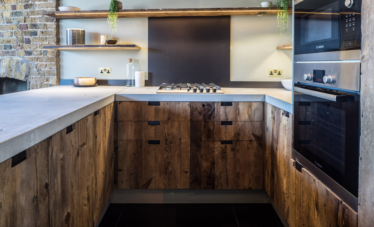 U-shaped kitchen with reclaimed barn wood cabinetry, concrete worktops, open timber shelves and exposed ceiling beams