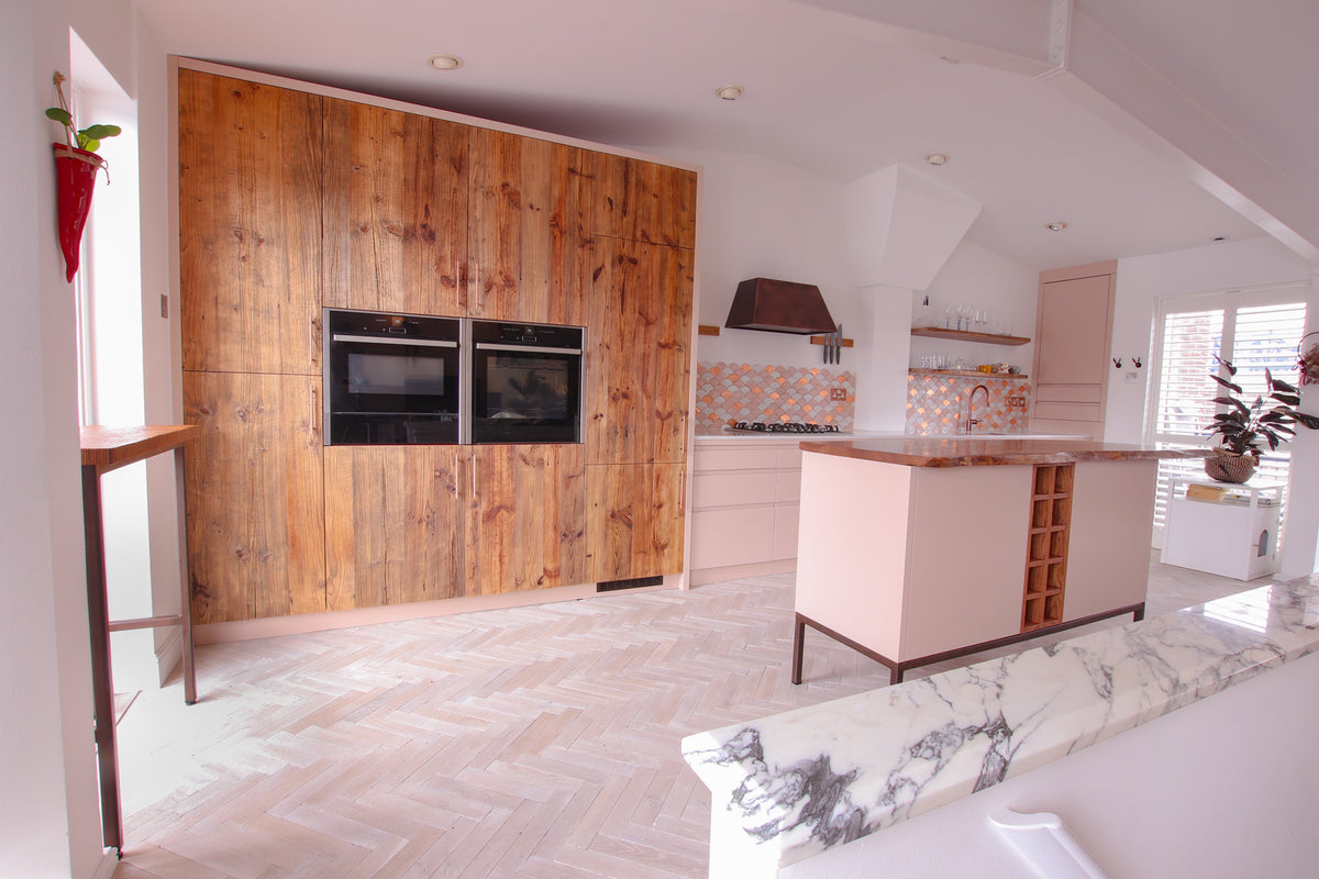 Tall kitchen unit clad in reclaimed barn wood with integrated double ovens, part of a blush and timber modern kitchen